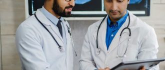 Two experienced gastroenterologists in white coats scrutinize the endoscopy results on a large medical monitor